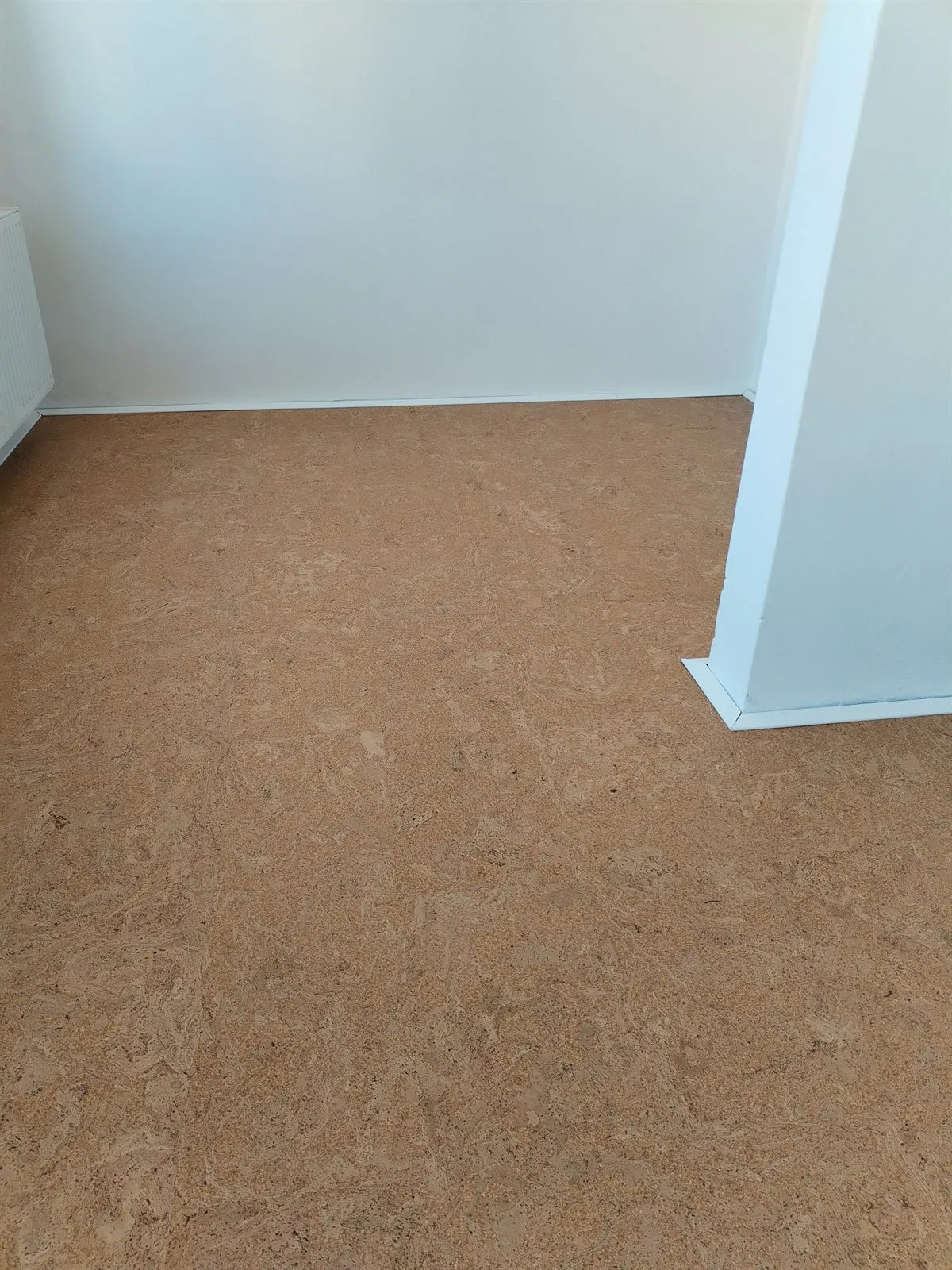 Nová korková podlaha položená v pokoji, u stěny bílá soklová lišta a radiátor