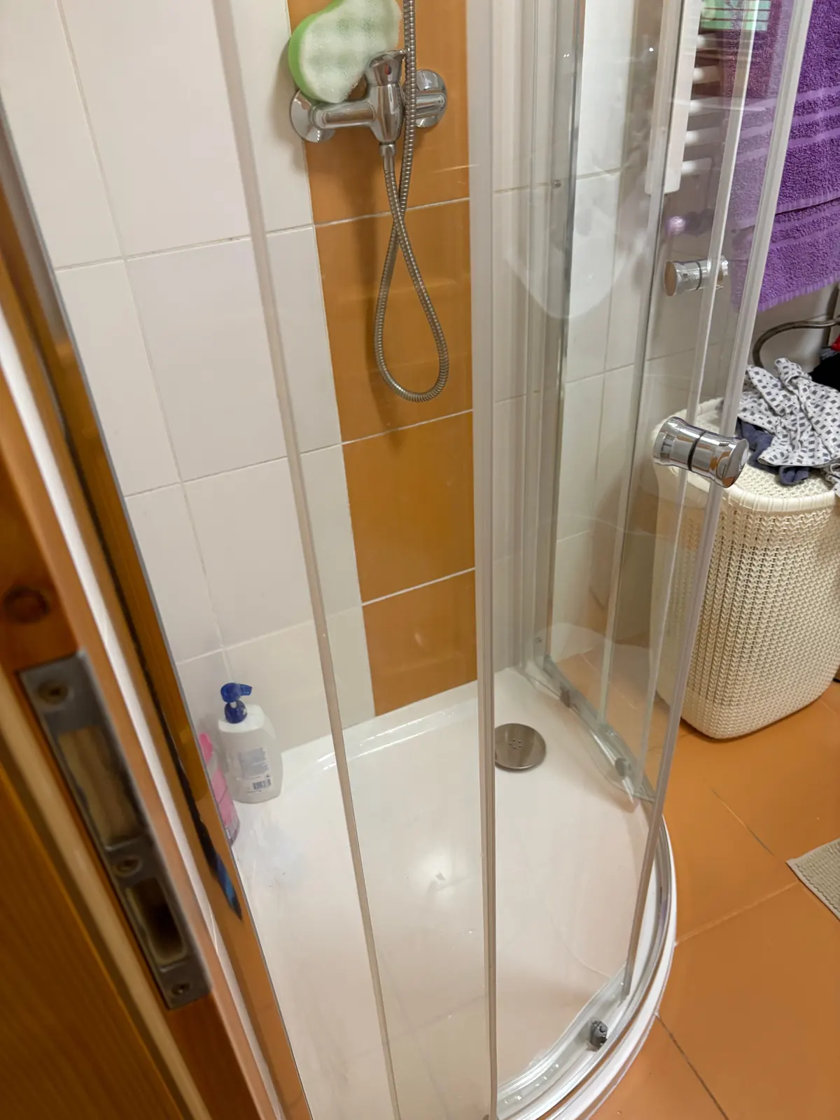 Čtvrtkruhový sprchový kout s posuvnými skleněnými dveřmi a bílou vaničkou, na obkladu nástěnná sprchová baterie